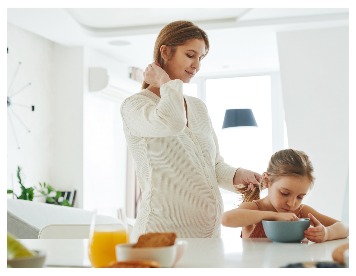 A pregnant mother braiding her young daughter's hair.