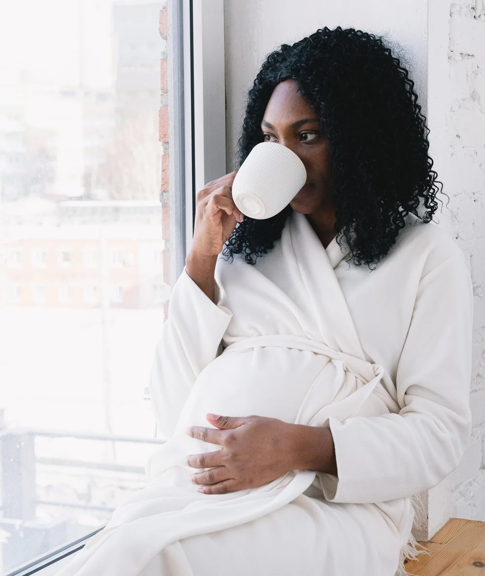 A pregnant woman holding her baby bump drinking tea.